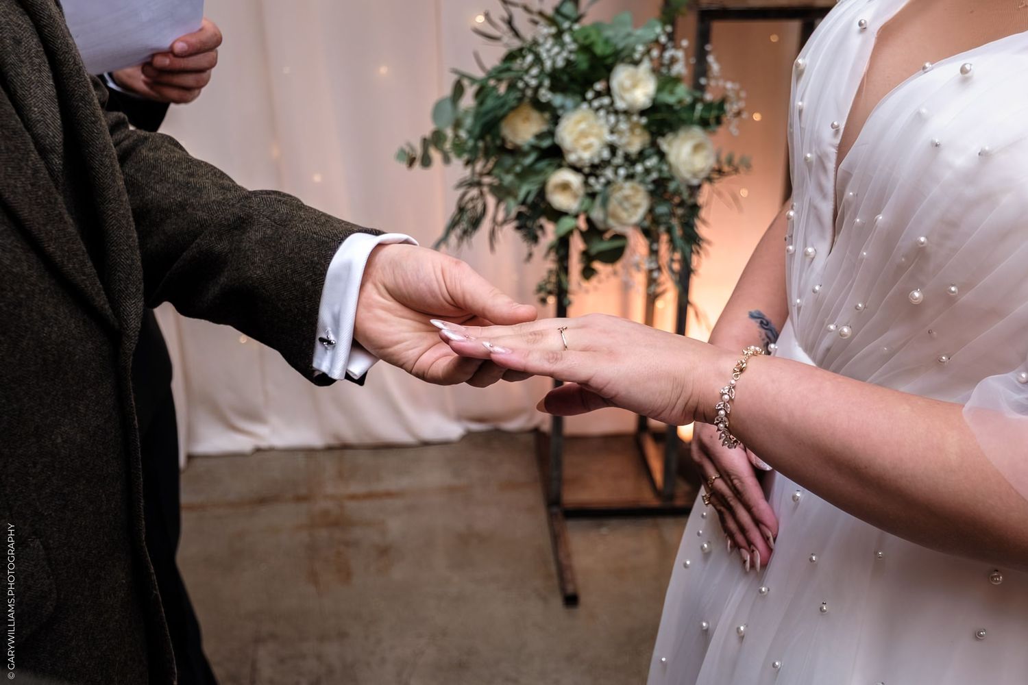 Close-up of hands exchanging wedding rings during ceremony with floral decor in background.