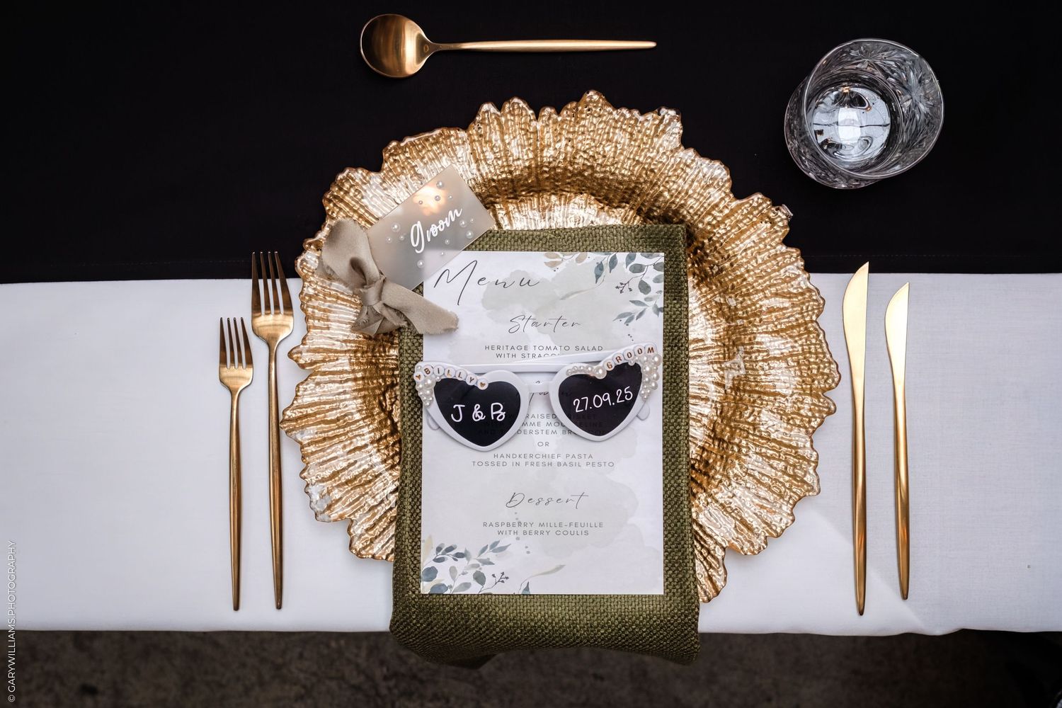 Elegant wedding table settings with gold cutlery, white plates, and rustic decor against a dark background.