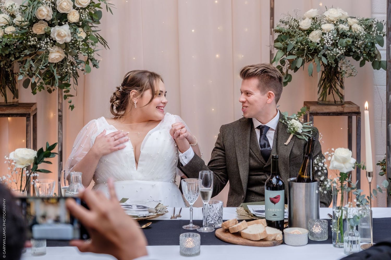Wedding couple shares intimate moments during their reception dinner with elegant floral decor and soft lighting.