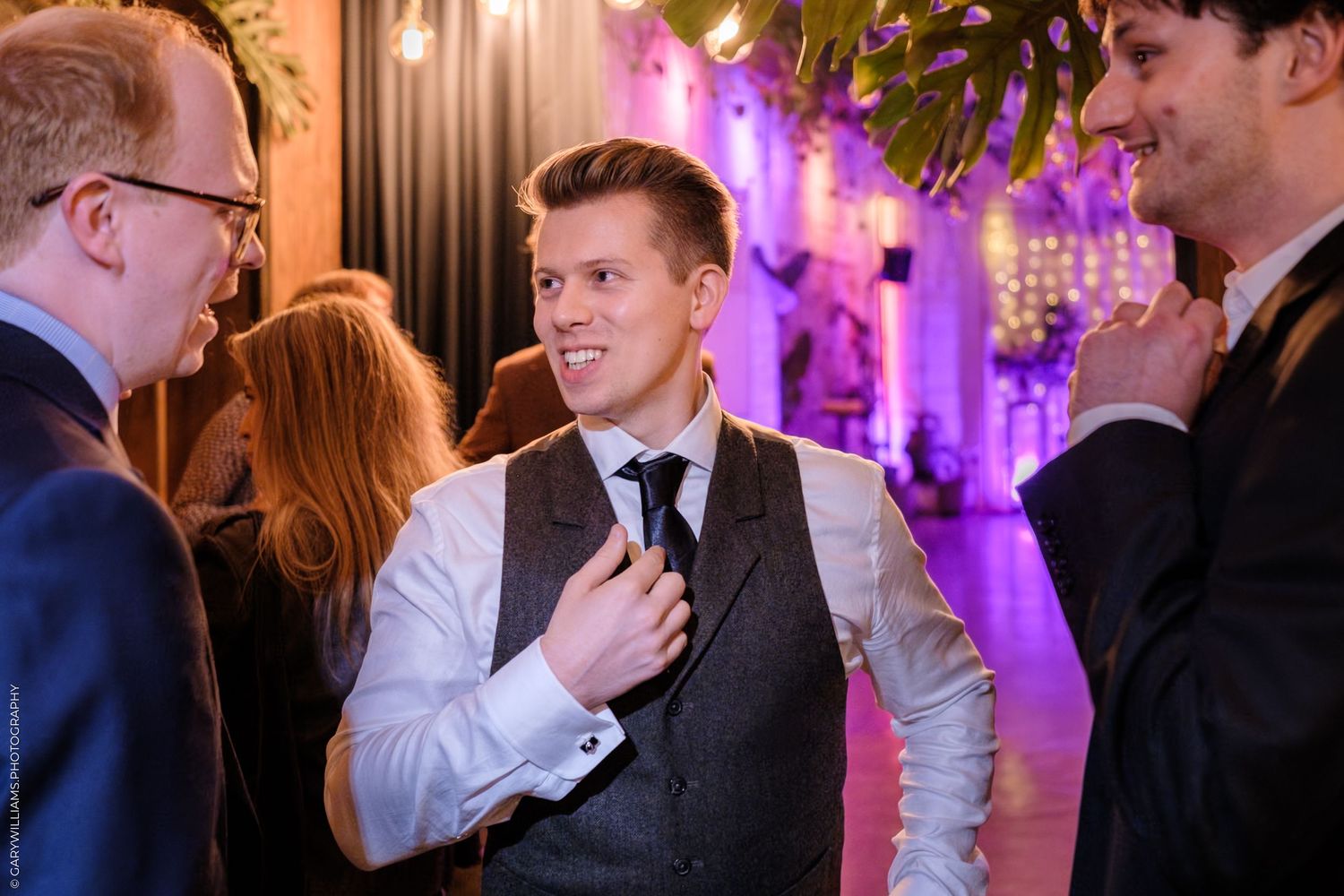 A group of people mingling and socializing at an elegant indoor event with purple ambient lighting.