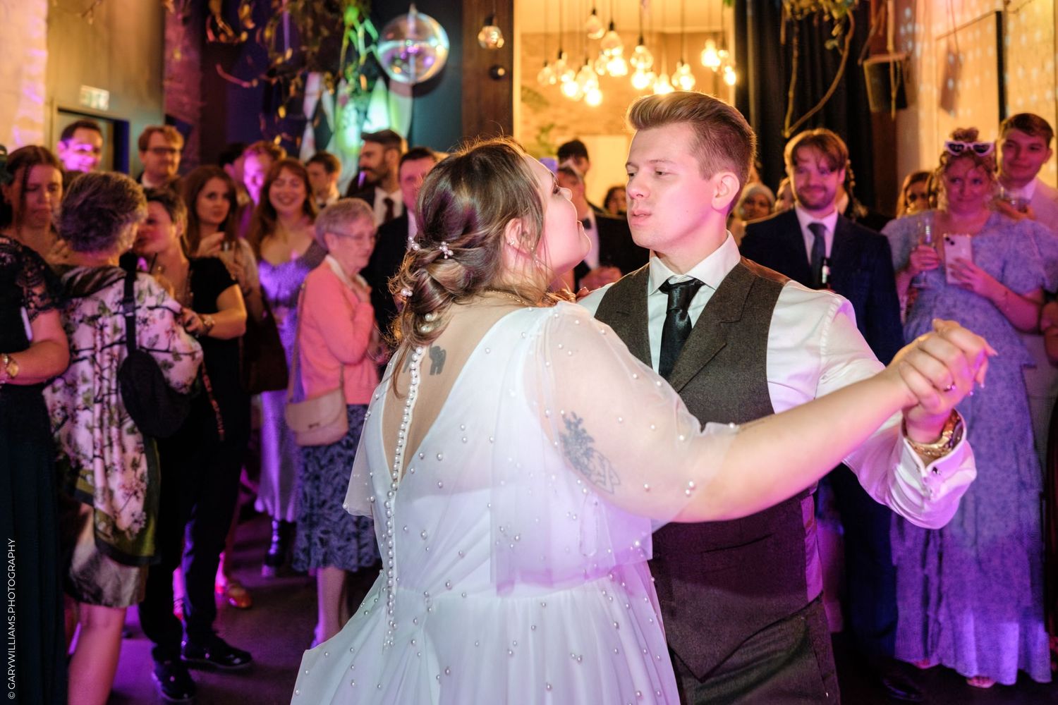 Wedding guests dance and celebrate on a lively reception dance floor illuminated with warm lighting.