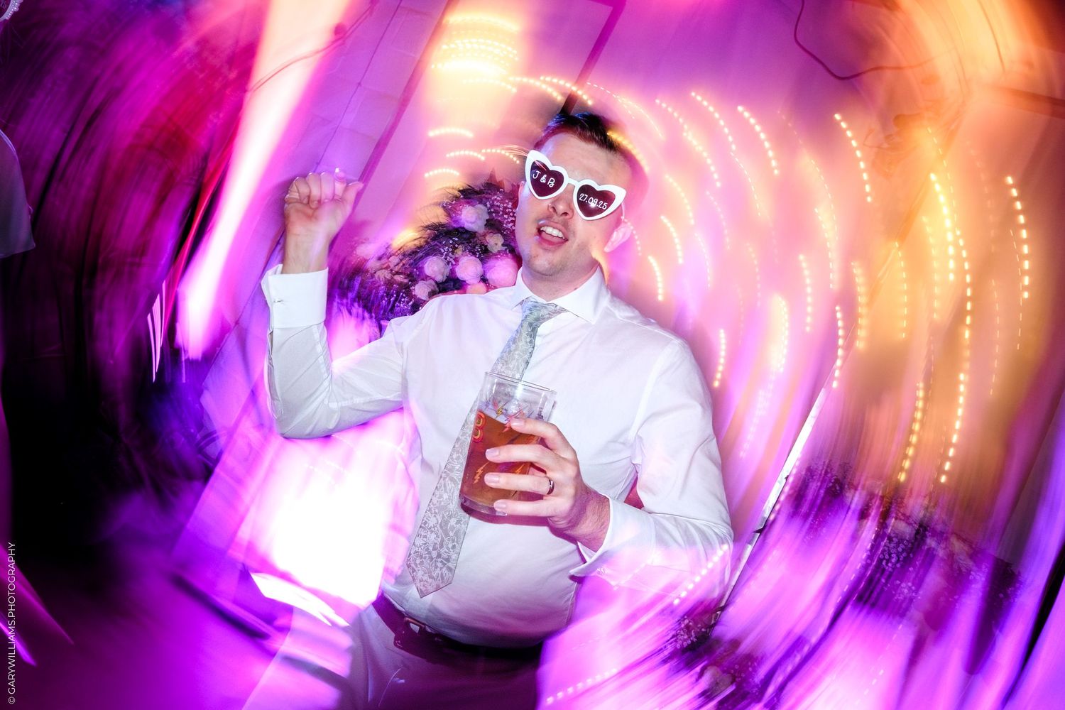 Dance floor filled with party guests under vibrant purple and pink lighting effects.