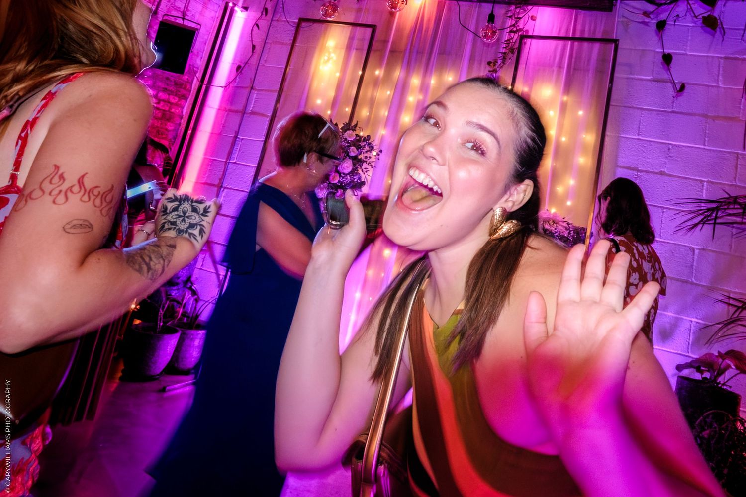 People dancing and celebrating at a lively party with pink and purple lighting creating an energetic atmosphere.