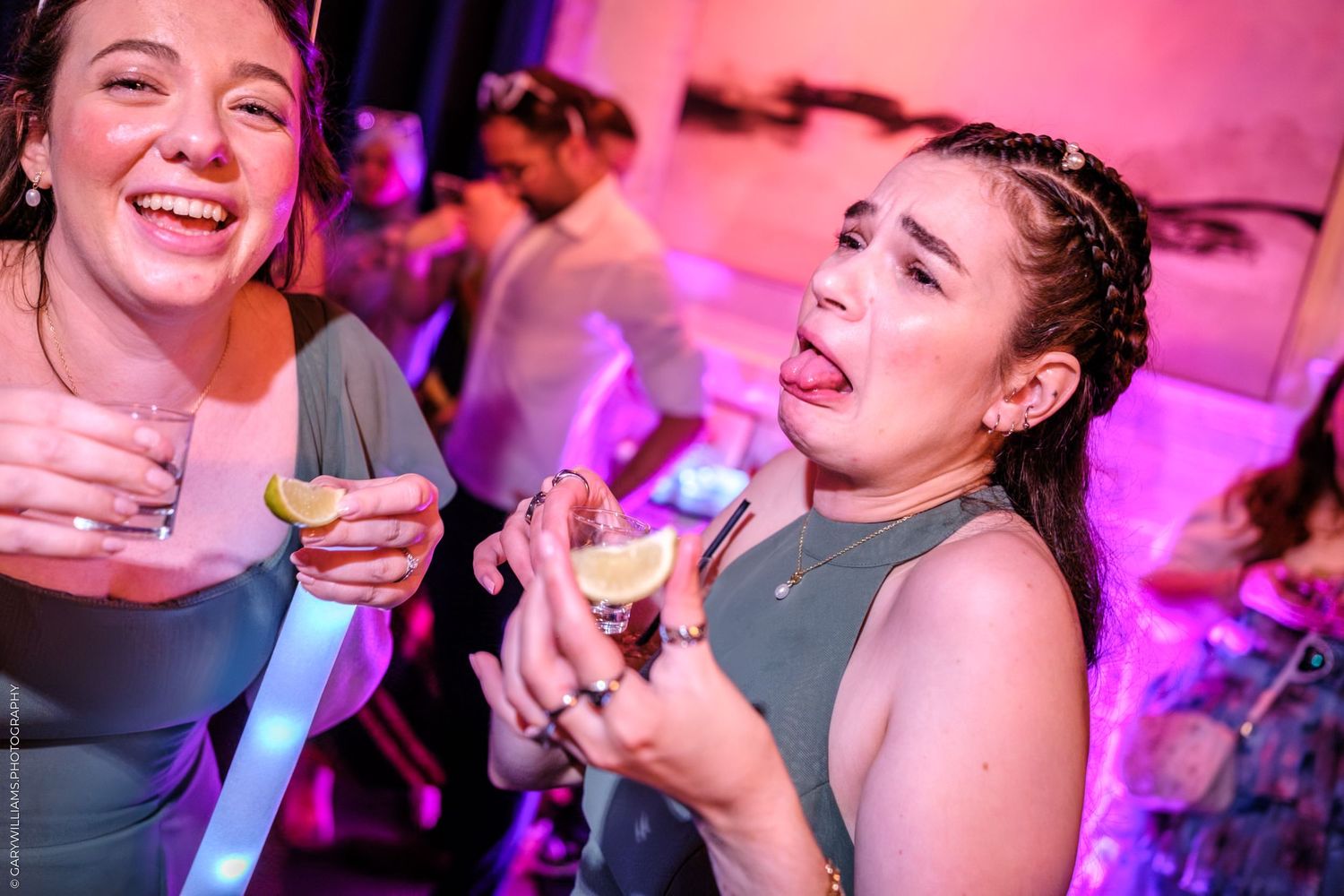 People dancing and celebrating at a lively party with pink and purple lighting in a nightclub setting.