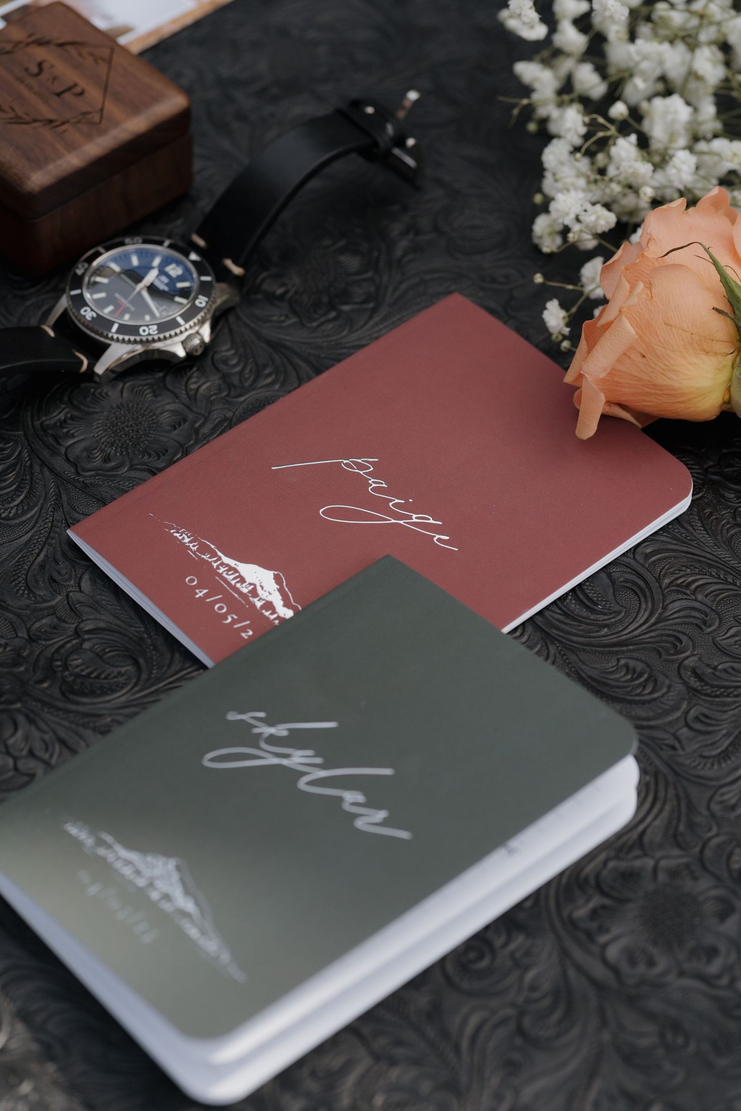 Wedding vow books or journals in burgundy and gray colors displayed with white flowers on dark textured surface. Leavenworth, WA