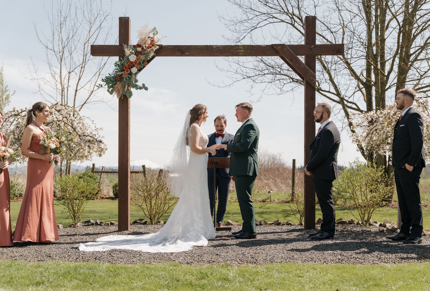 Wedding party members pose outdoors near a rustic wooden cross during a spring ceremony. Leavenworth, WA