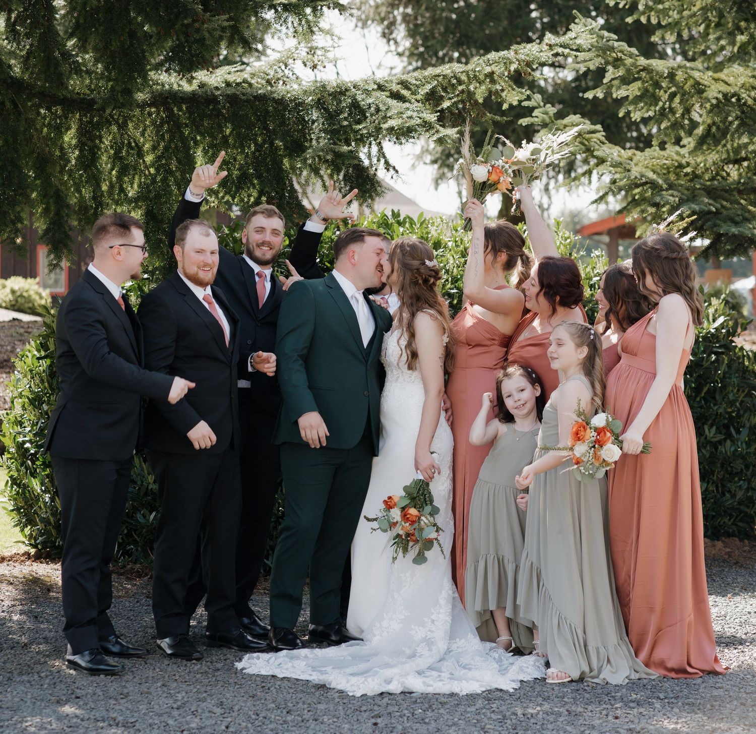 Wedding party in peach and gray dresses gather for formal photos under green trees. Leavenworth, WA