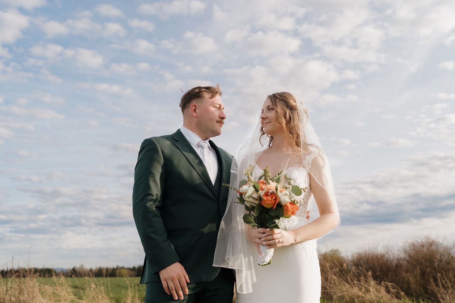 Wedding couple standing together in a field under cloudy blue sky. Leavenworth, WA
