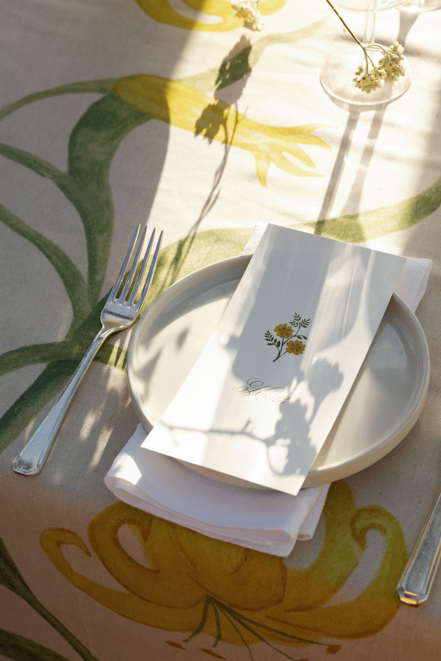 A series of table place settings with white plates and napkins cast shadows in natural sunlight against a yellow patterned surface.