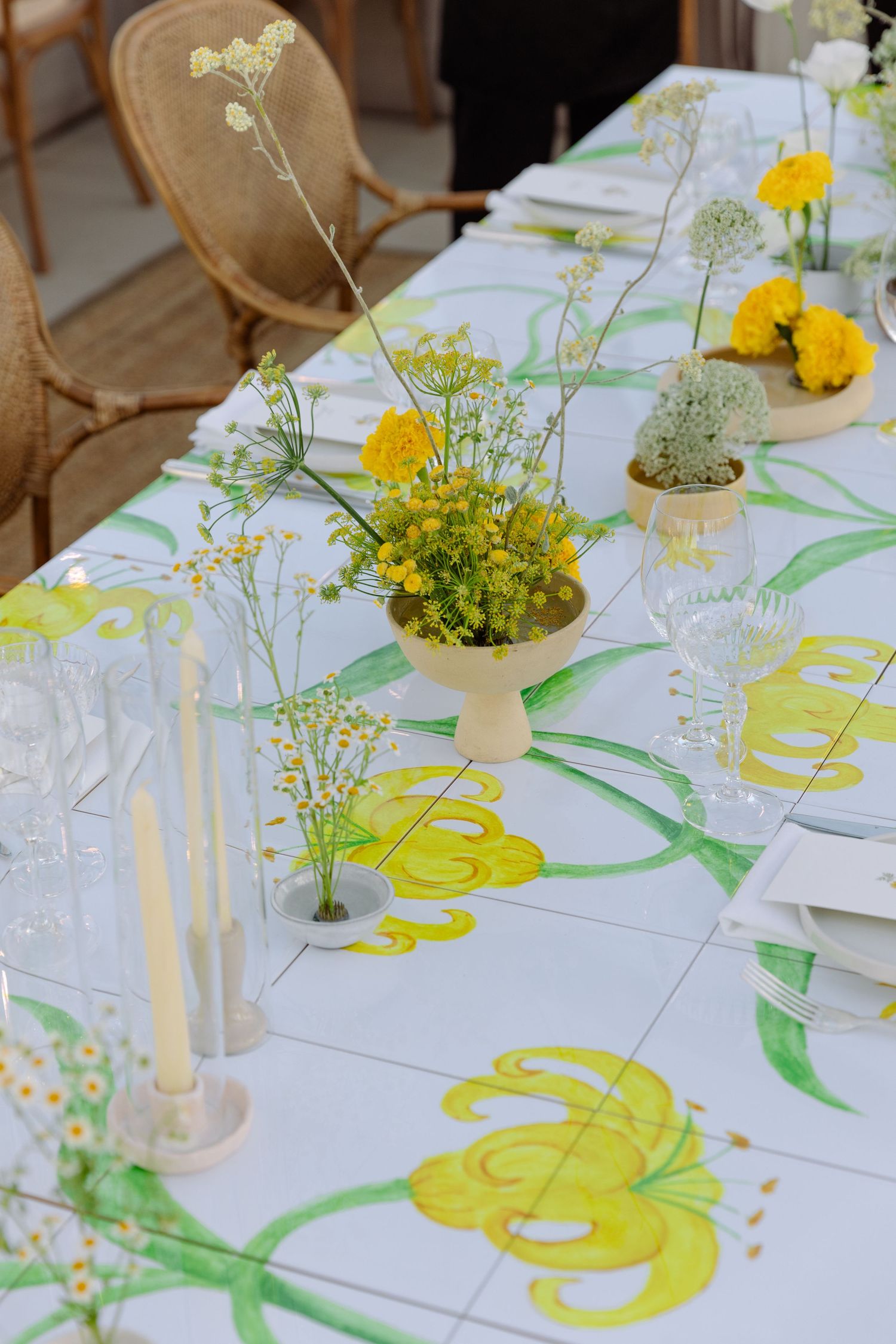 Elegant table setting with yellow and white wildflowers in vases on a floral patterned tablecloth with taper candles.