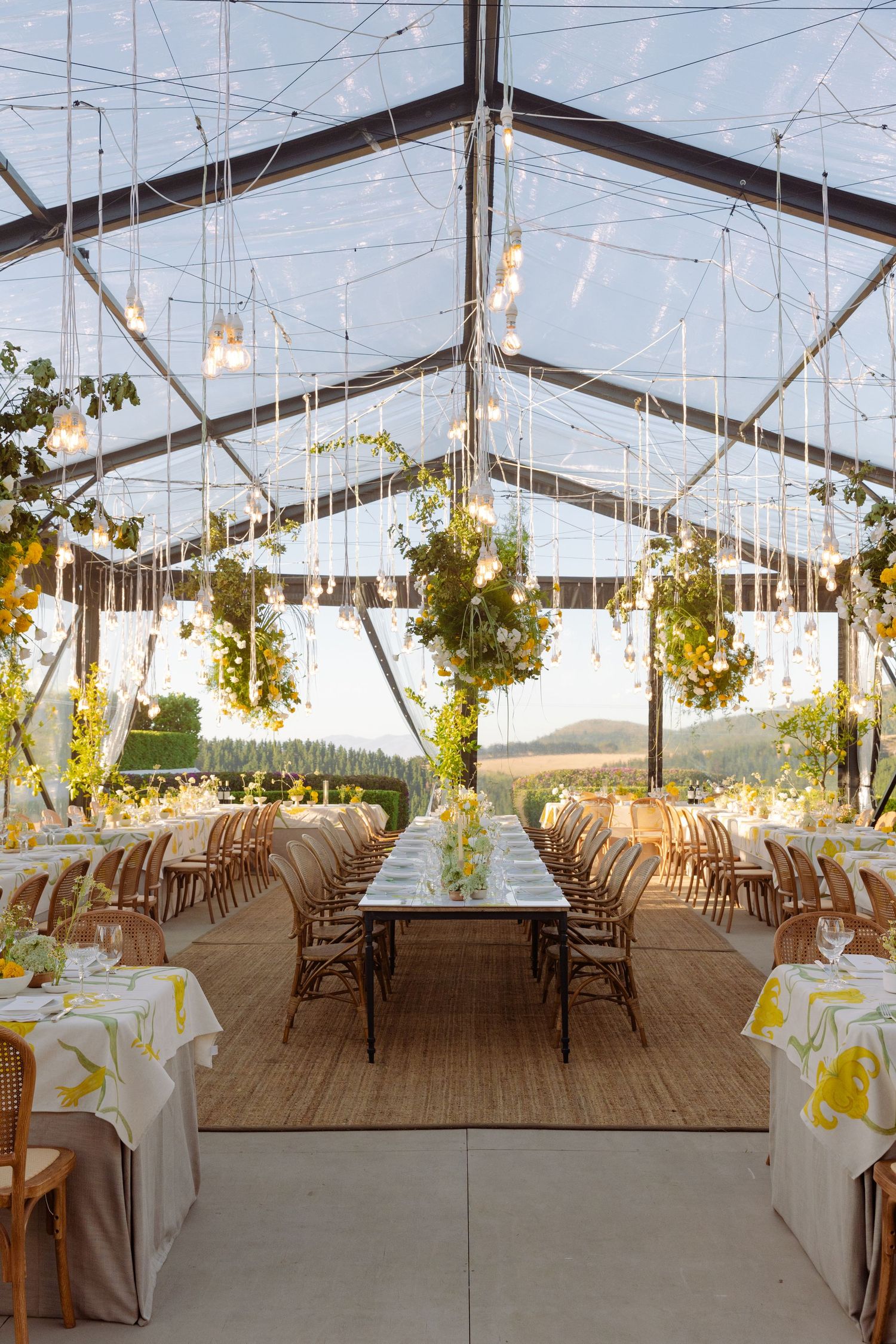 Clear tent wedding reception setup with long wooden tables and string lights creating an elegant outdoor atmosphere.