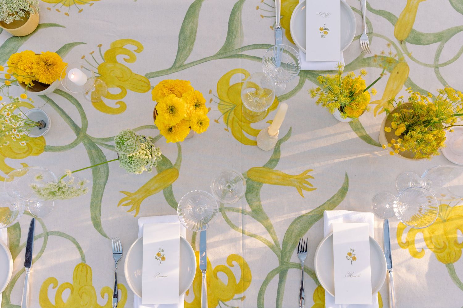 Illuminated yellow floral decorations and delicate greenery hang from a ceiling creating an enchanting garden atmosphere.