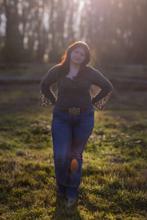 Person in blue jeans stands in golden sunlit field during sunset creating a warm atmospheric scene.