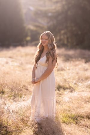A person in a flowing white dress stands in a sun-drenched field during golden hour creating a dreamy atmosphere.