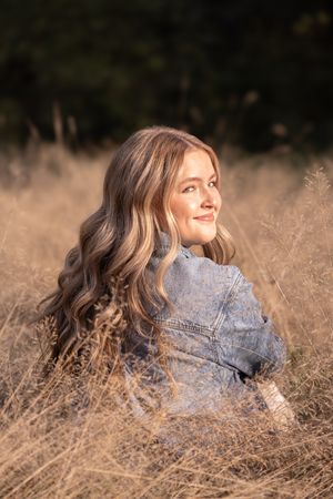 A person lies in golden dry grass wearing denim while looking up at the sky in a dreamy outdoor portrait series.