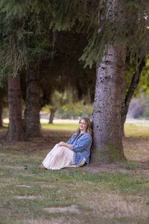 Person relaxes under tall evergreen trees in a peaceful outdoor setting wearing casual denim and white clothing.