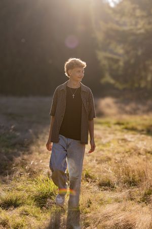 Child walks through golden sunlit field wearing plaid shirt and jeans during sunset.