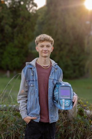Someone in a denim jacket holds a vintage Gameboy device while standing outdoors at sunset.