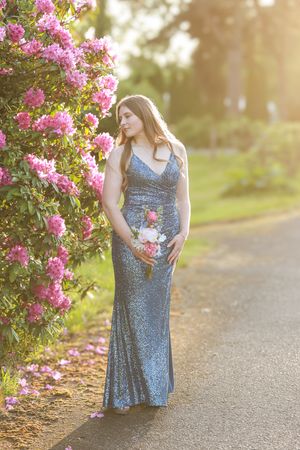 Sparkling blue evening gown photographed at sunset next to blooming pink flowers along a garden path.