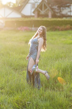 A person in a floral dress poses playfully in a sunlit grassy field during golden hour.