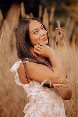 A woman in a floral dress poses gracefully in a field of dried grass during golden hour.