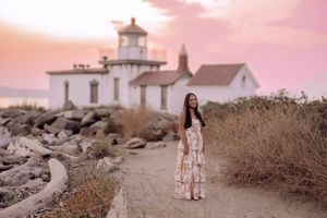 A dreamy coastal lighthouse scene at sunset with a path leading through brown grass and rocks.