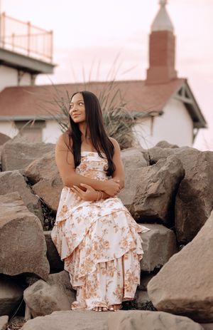 A series of sepia-toned photos showing someone in a floral dress posing on rocky coastal boulders at sunset.