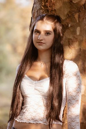 A person in a white lace top poses against a soft autumn background with bokeh lighting effects.