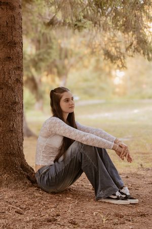A casual portrait session under a tree shows someone sitting on brown pine needles in soft golden light.