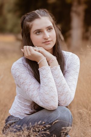 A person in a white lace top sits thoughtfully in a field of golden grass at sunset.