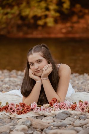 A dreamy outdoor photo shoot features pink roses arranged on smooth river rocks in warm autumn lighting.