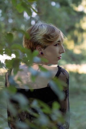 A person in a black top poses behind green foliage in a dreamy outdoor photoshoot series.