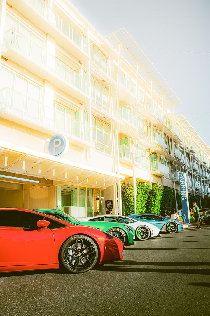 Colorful luxury supercars including red and green models displayed in a row at an upscale venue.