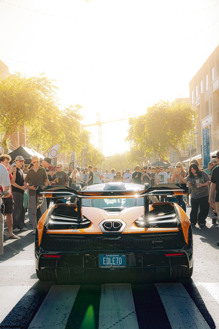 Rear view of a McLaren sports car with distinctive taillights and aerodynamic design drawing crowds at dusk.