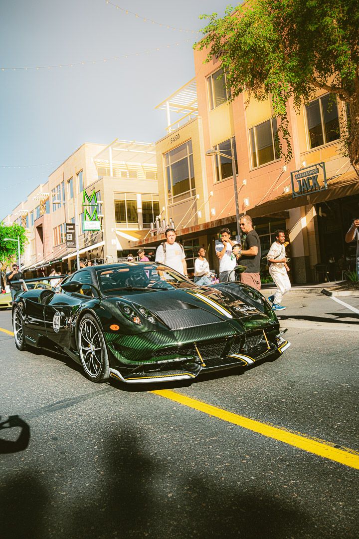 Line of exotic sports cars displayed on a sunny street with palm trees and buildings in background.
