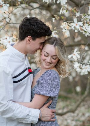 Couple embraces tenderly under blooming white cherry blossoms in springtime setting.