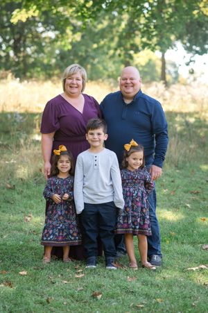 Family poses together on grassy hillside during outdoor autumn photo session.