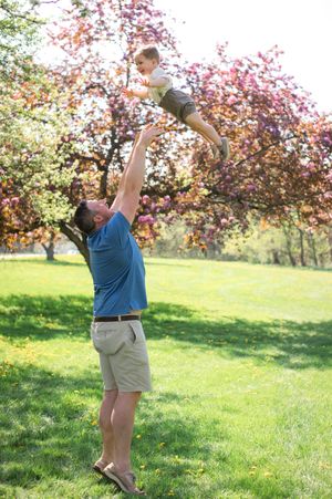 Person in blue shirt and khaki shorts jumping for joy in a blooming orchard on a sunny spring day.