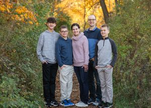 Family group poses together outdoors during autumn with colorful fall foliage in the background.