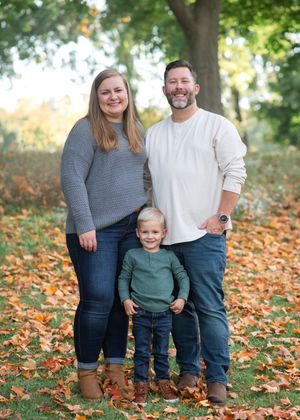A family poses together in autumn leaves wearing coordinated blue and white outfits for a casual outdoor photoshoot.