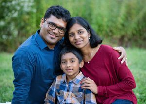 A family wearing blue and burgundy outfits poses together outdoors for a series of casual portraits in nature.
