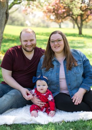 Family sitting on white blanket outdoors during autumn photoshoot with baby in red outfit.