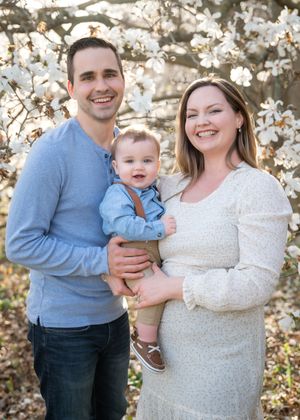 A couple and their baby pose together in front of blooming white cherry blossoms during a spring photo session.