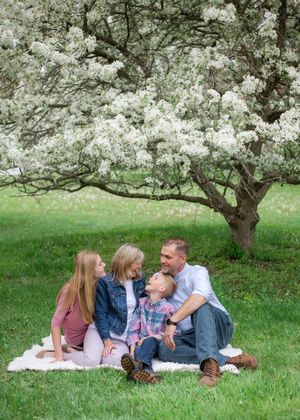 A family lies together on a blanket under blooming white cherry blossom trees in springtime.