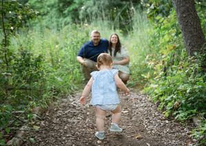 A group walks along a winding dirt trail through lush green forest vegetation on a summer day.