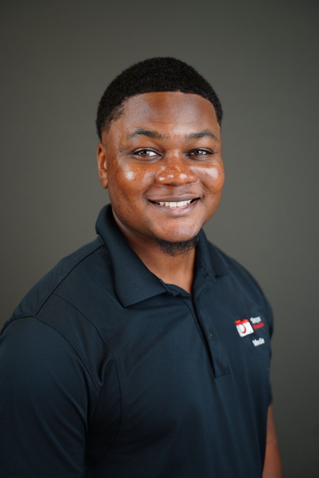 Professional studio portraits of someone wearing a dark polo shirt with a company logo against a gray background.