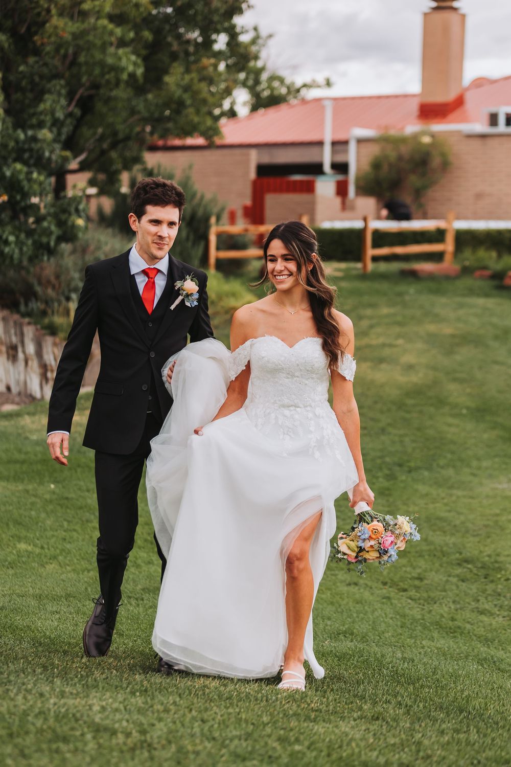 A couple walks on green grass during their outdoor wedding, with the bride in a white dress holding a colorful bouquet.