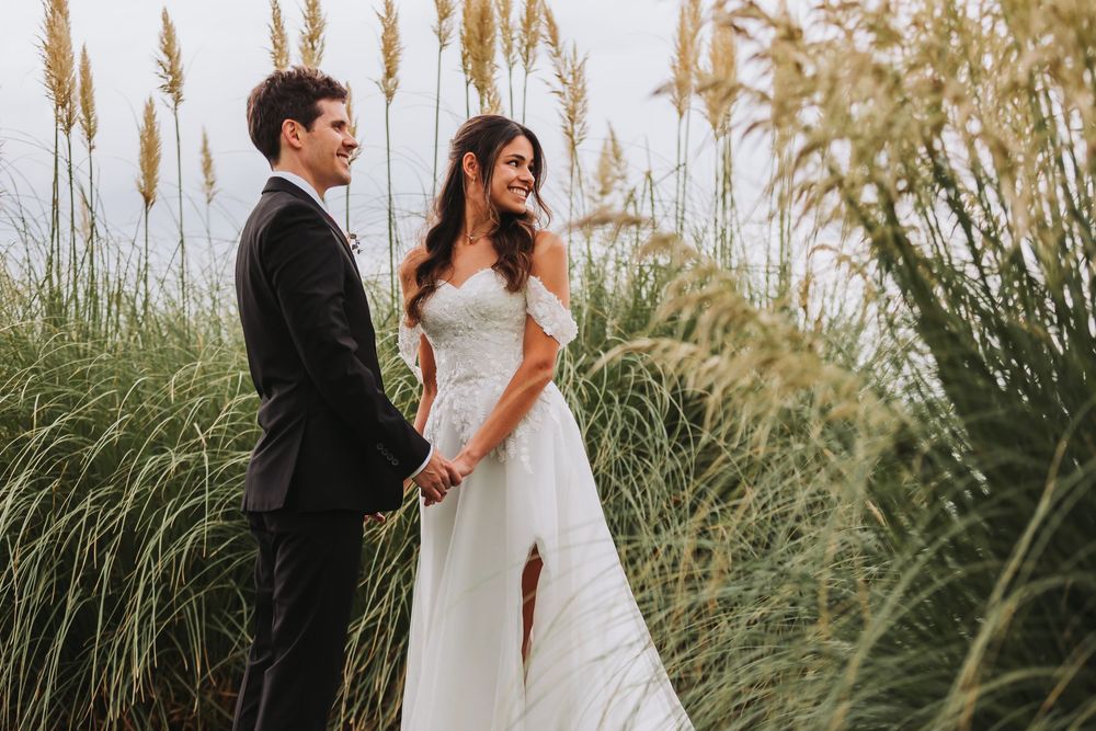 Couple in wedding attire embraces among tall ornamental grasses during golden hour outdoor photoshoot.