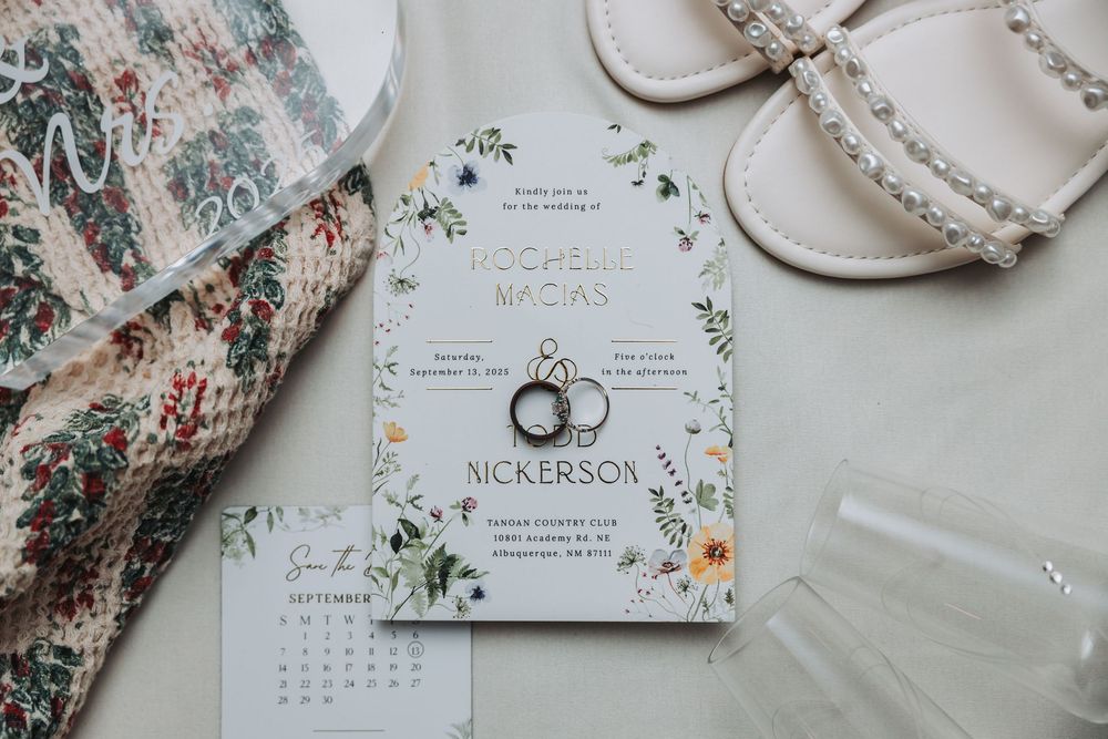Wedding invitation suite with floral pattern fabric, calendar, and elegant paper details laid out on light surface.