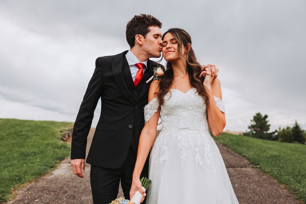 A couple in formal wedding attire shares a romantic moment together on a scenic outdoor path.